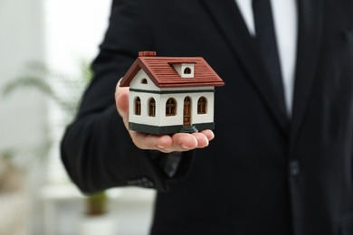 Photo of Real estate agent holding house model indoors, closeup