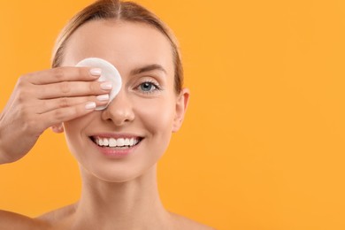 Photo of Smiling woman removing makeup with cotton pad on yellow background, closeup. Space for text