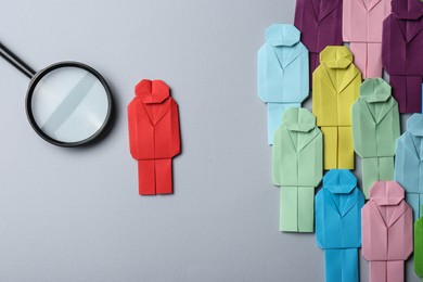 Photo of Many colorful paper figures and magnifying glass on grey background, flat lay. Recruiter searching employee