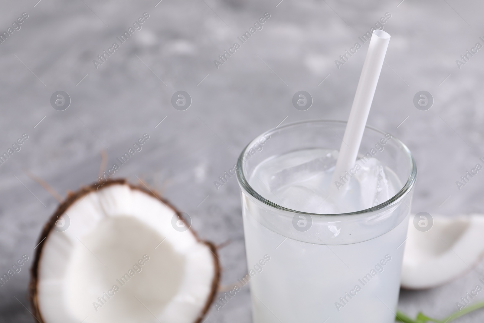 Photo of Glass of coconut water with ice cubes on grey table, closeup