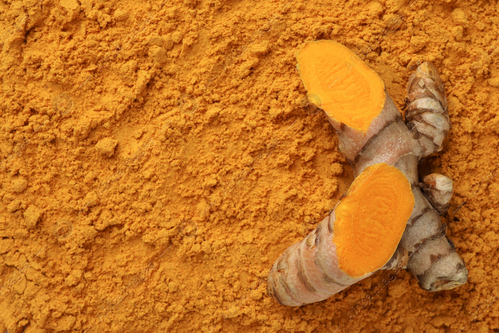 Photo of Cut raw root on aromatic turmeric powder, top view. Space for text