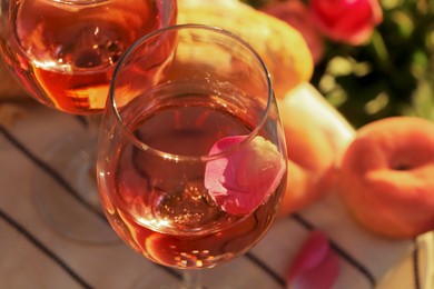 Photo of Glass of delicious rose wine with petals outside, closeup