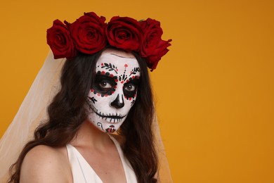 Photo of Young woman in scary bride costume with sugar skull makeup and flower crown on orange background, space for text. Halloween celebration