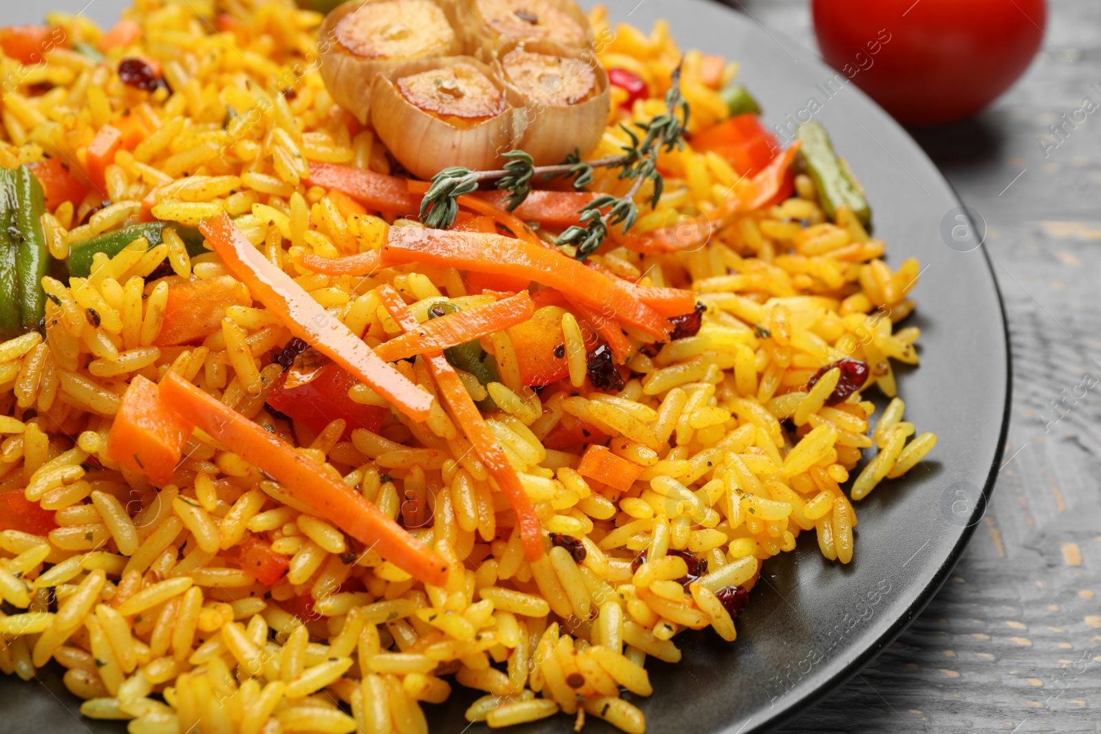 Photo of Tasty rice pilaf with vegetables on grey wooden table, closeup