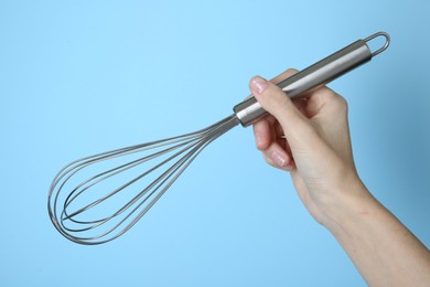 Photo of Woman holding metal whisk on light blue background, closeup