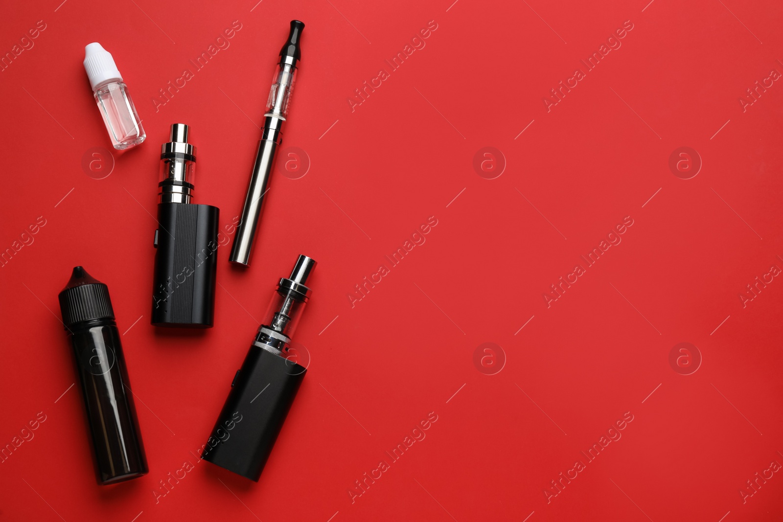 Photo of Many electronic smoking devices and vaping liquid on red background, flat lay. Space for text