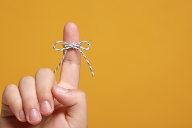 Man showing index finger with tied bow as reminder on orange background, closeup. Space for text