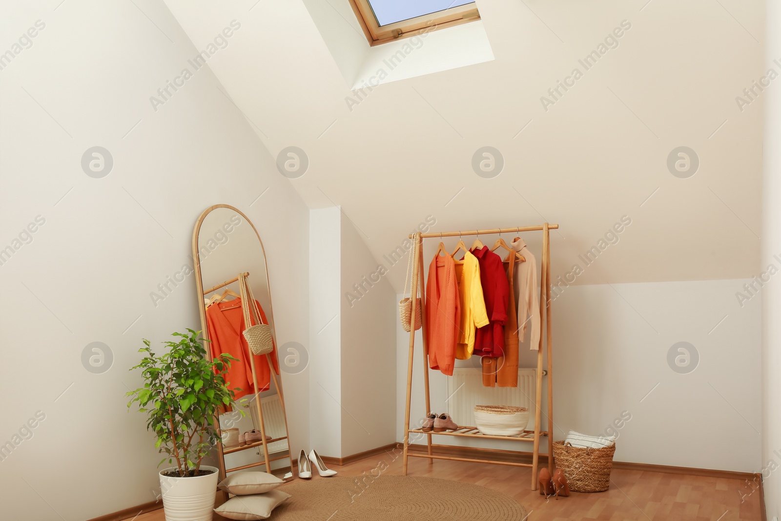 Photo of Stylish clothes rack, mirror and houseplant in room. Interior design