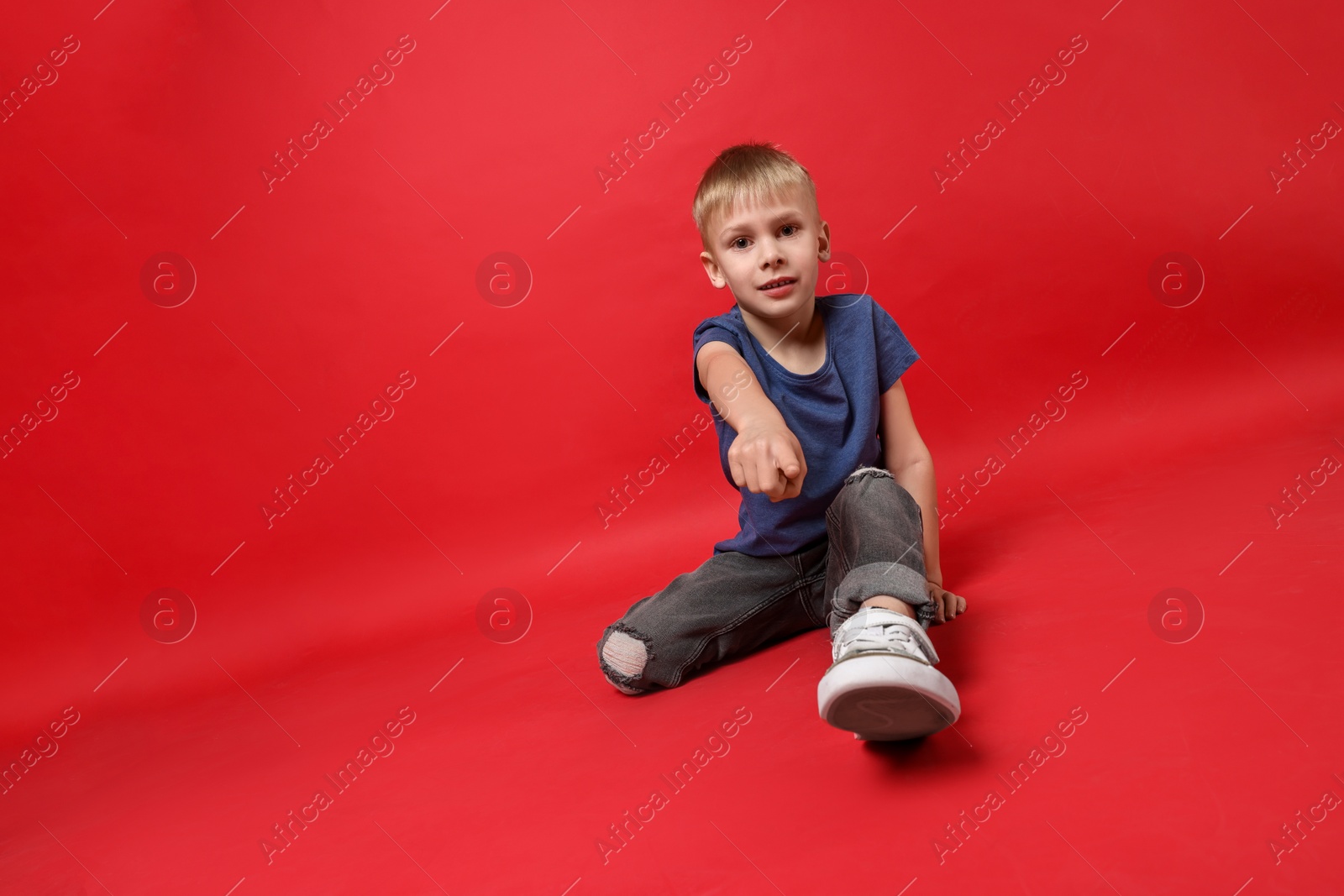 Photo of Happy little boy dancing on red background. Space for text