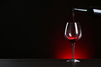 Photo of Pouring wine from bottle into glass on table against dark background, space for text
