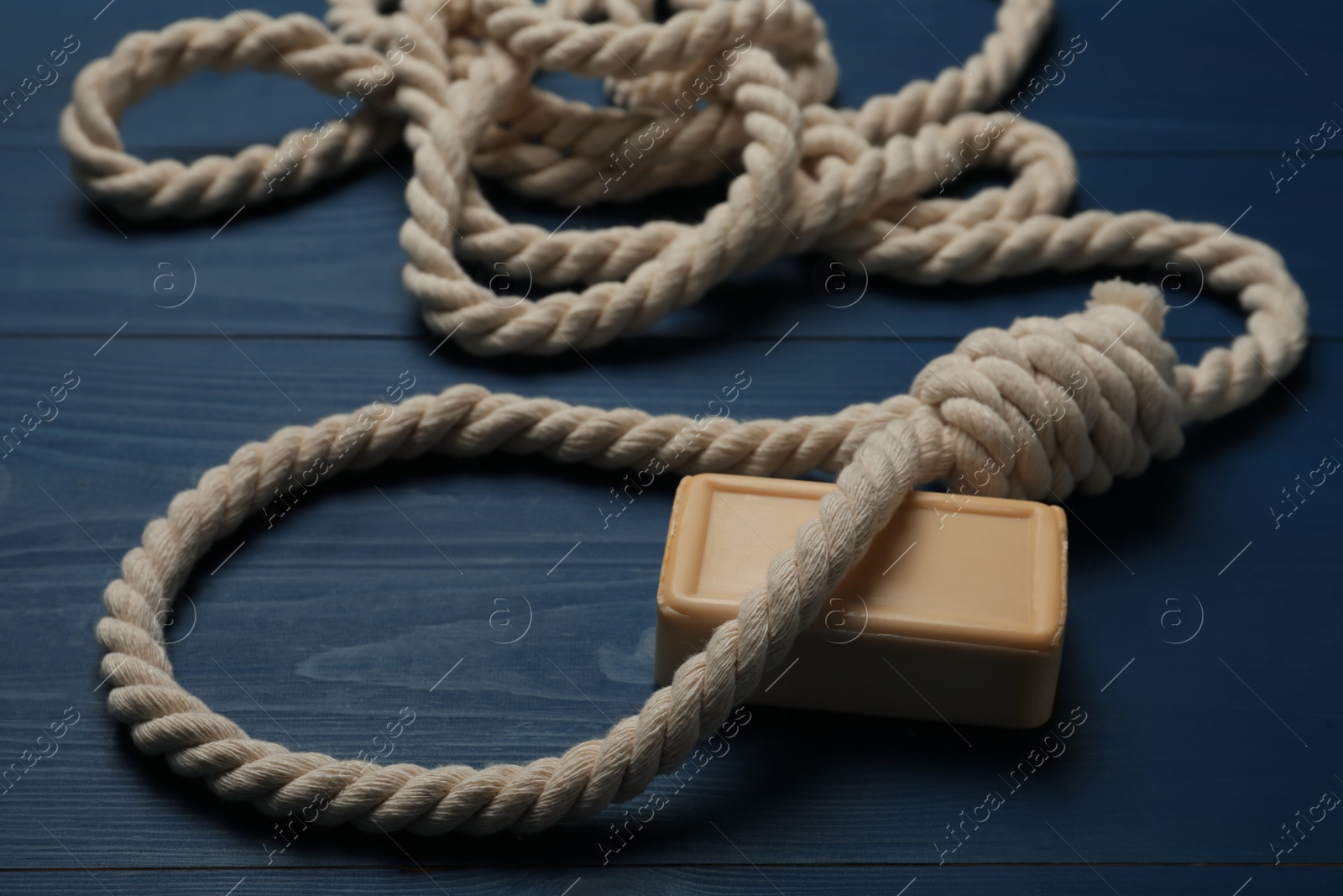 Photo of Rope noose and soap bar on blue wooden table, closeup
