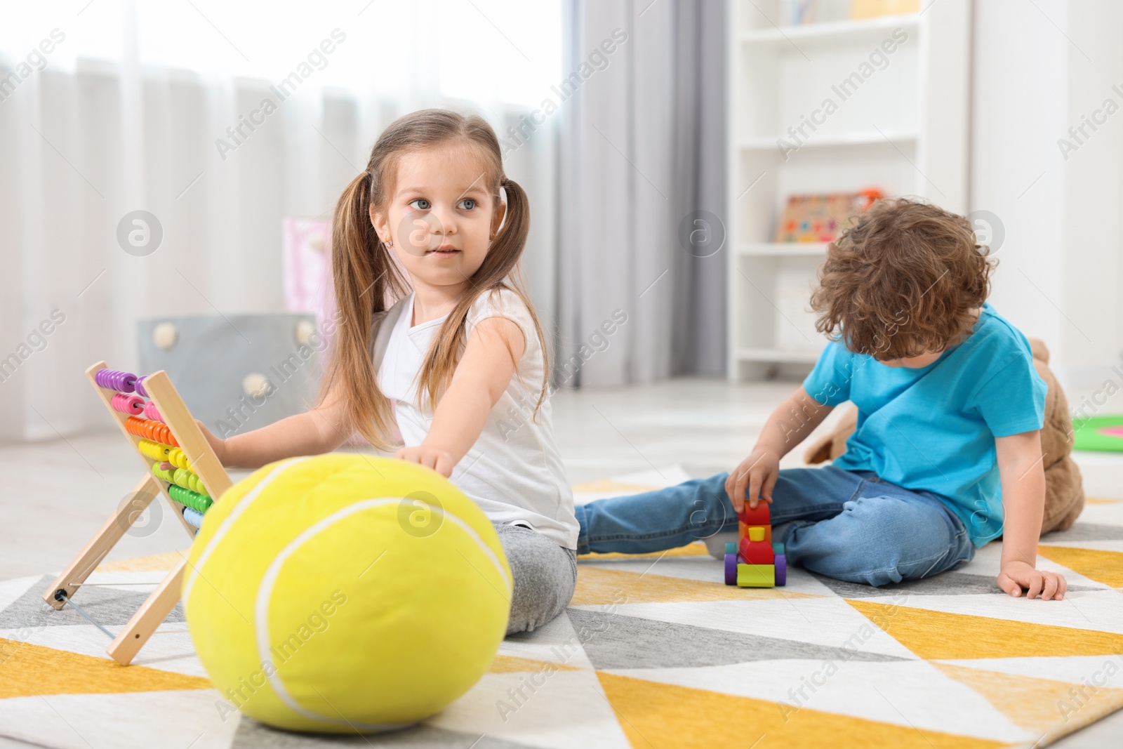 Photo of Cute little children playing with different toys on floor in kindergarten