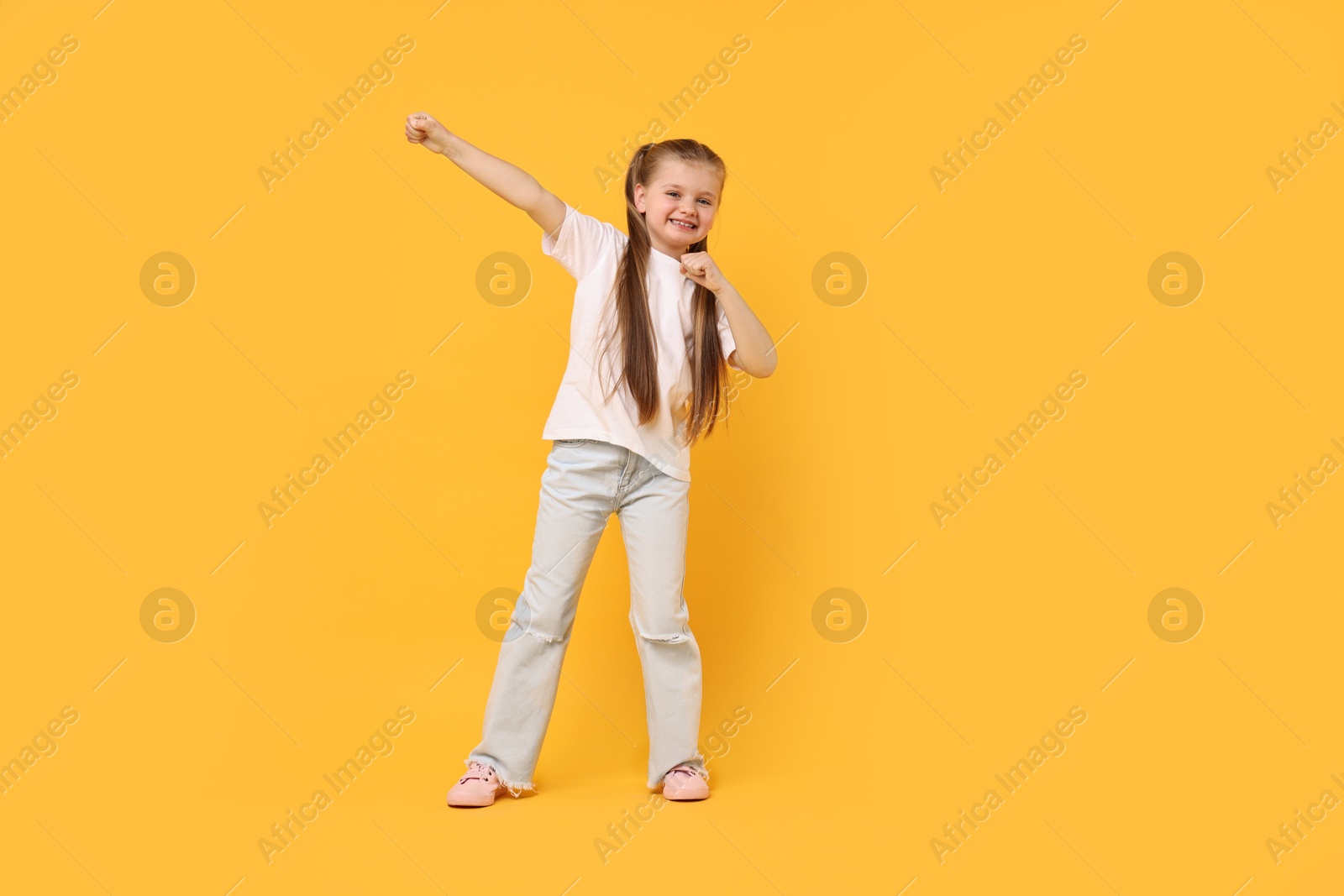 Photo of Cute little girl dancing on yellow background, space for text