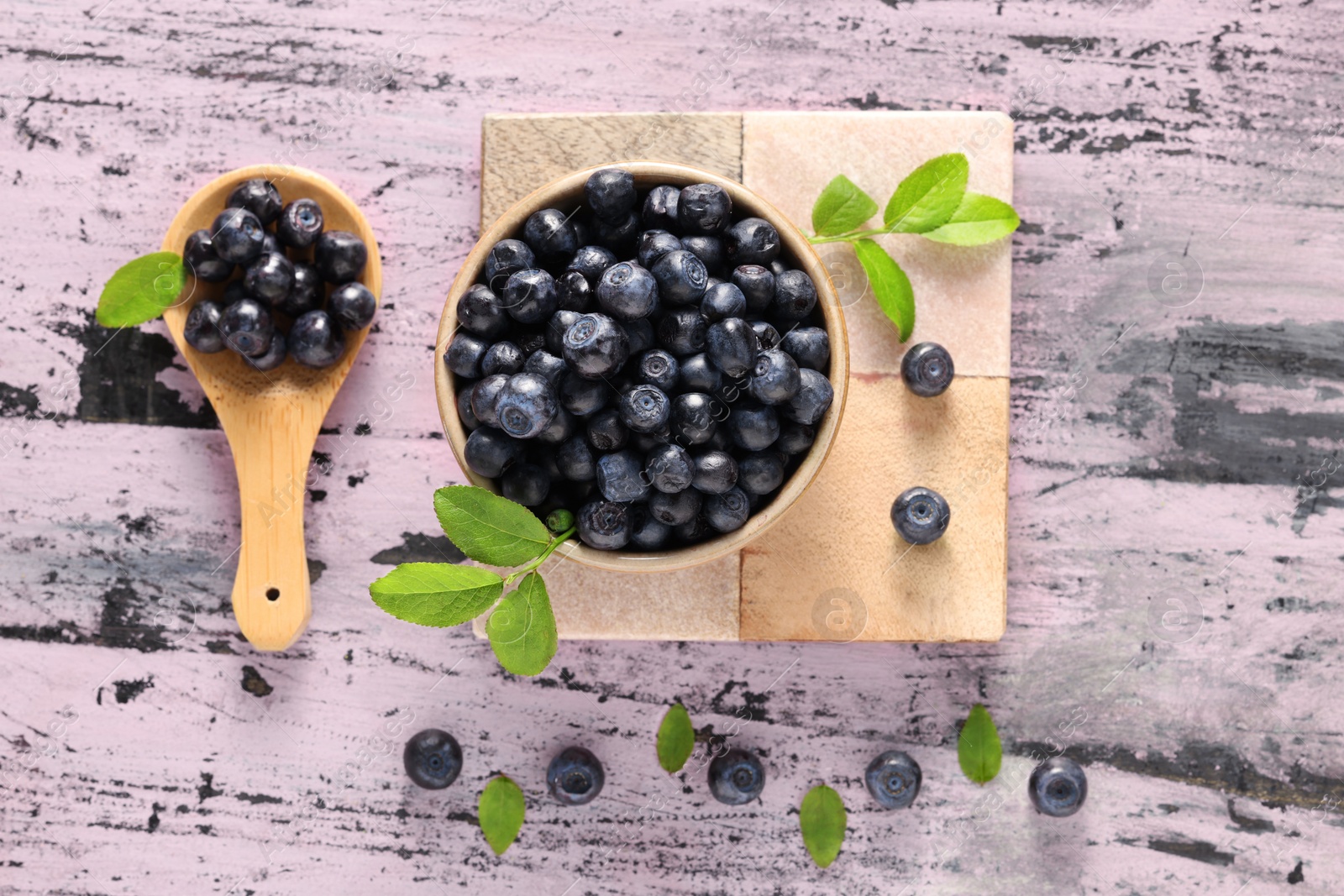 Photo of Tasty fresh bilberries and green leaves on old pink wooden table, flat lay