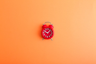 Modern alarm clock on orange background, top view