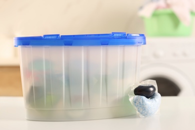 Photo of Laundry container and washing detergent capsule on table indoors