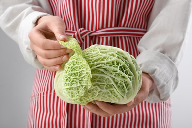 Photo of Woman separating leaf from fresh savoy cabbage on light grey background, closeup