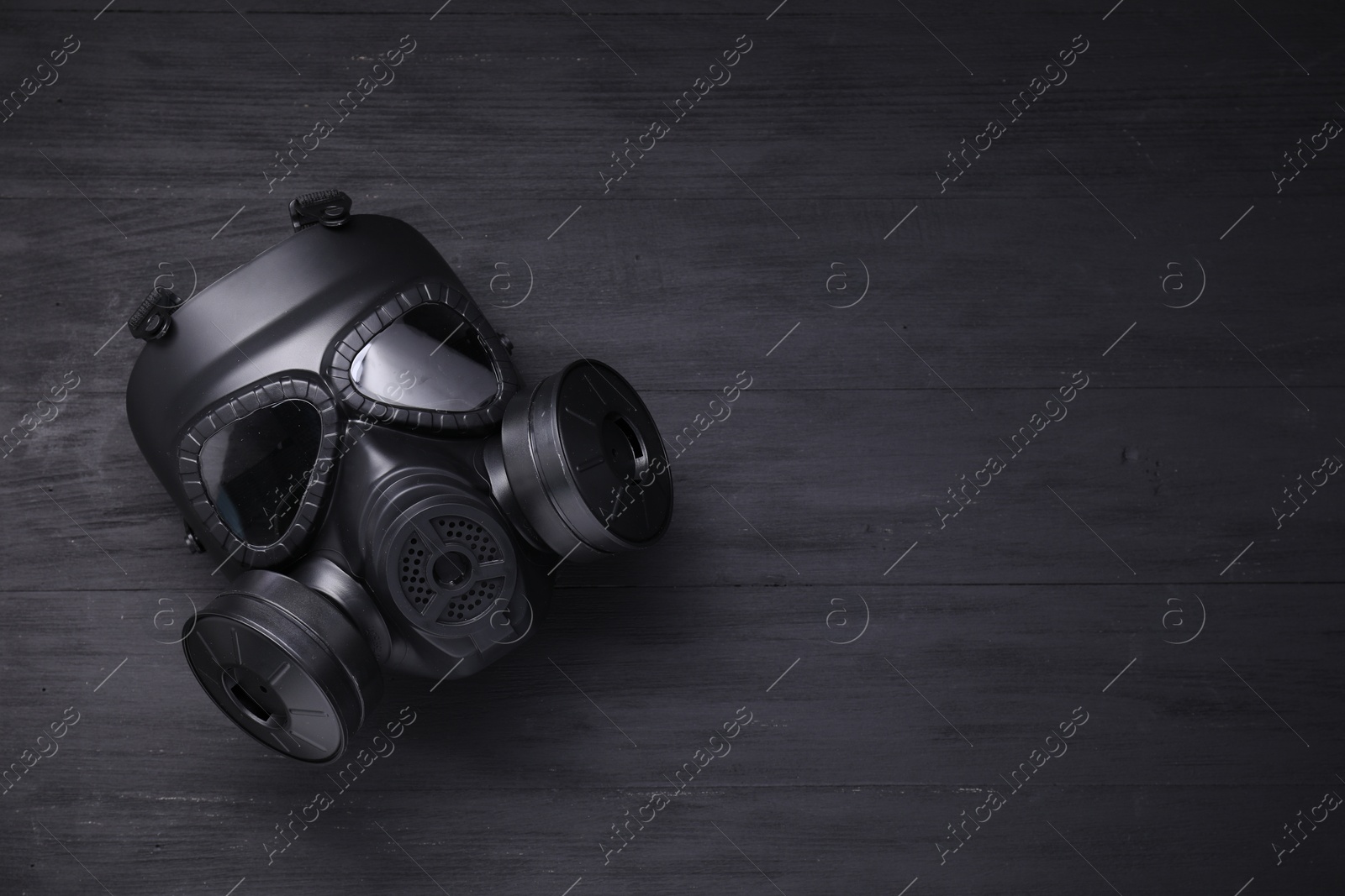 Photo of One gas mask on black wooden background, top view. Space for text