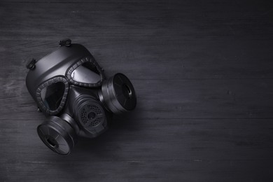 One gas mask on black wooden background, top view. Space for text