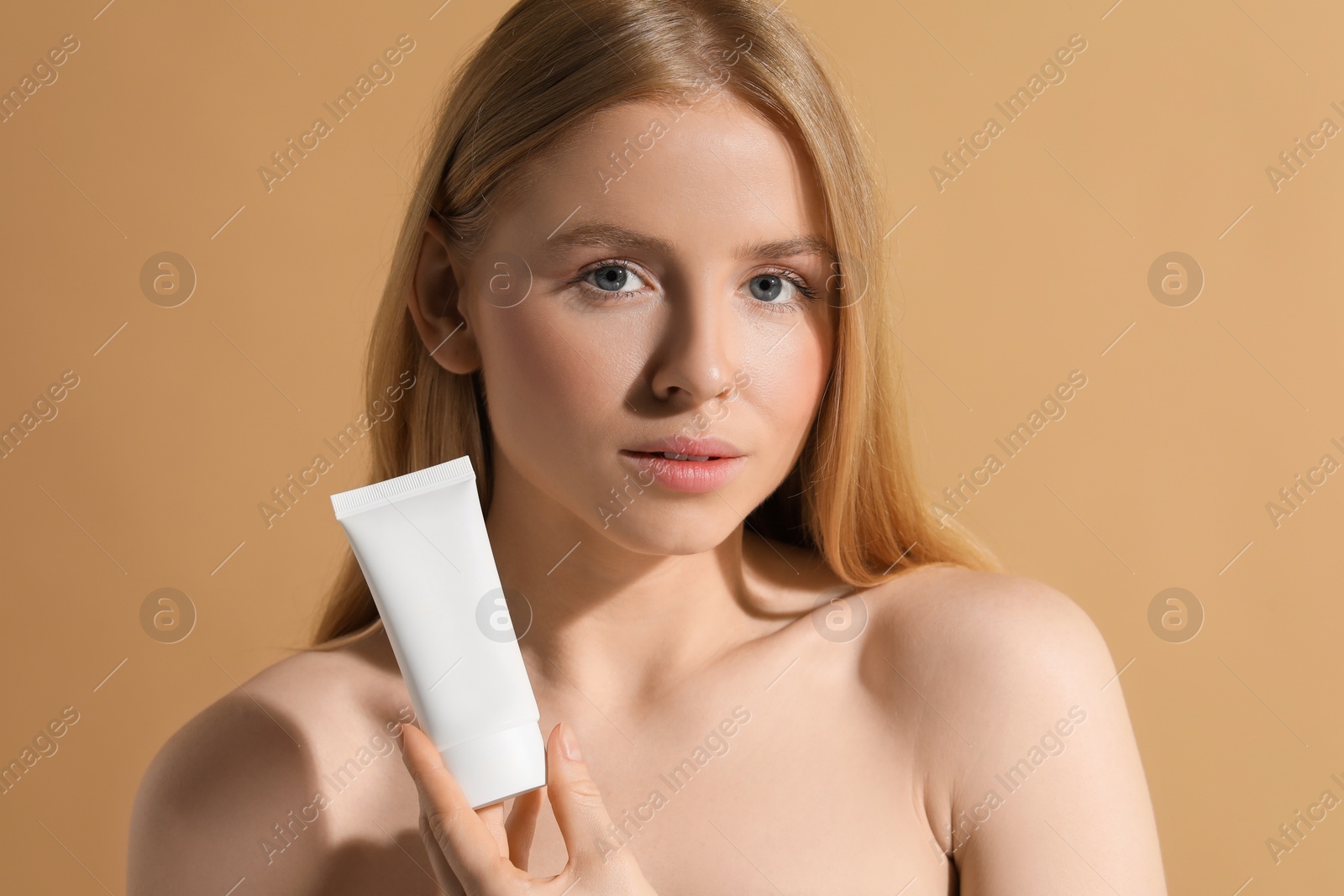 Photo of Beautiful young woman holding sun protection cream on beige background