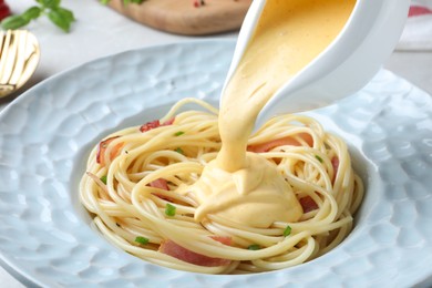 Photo of Pouring tasty cheese sauce onto spaghetti with meat, closeup