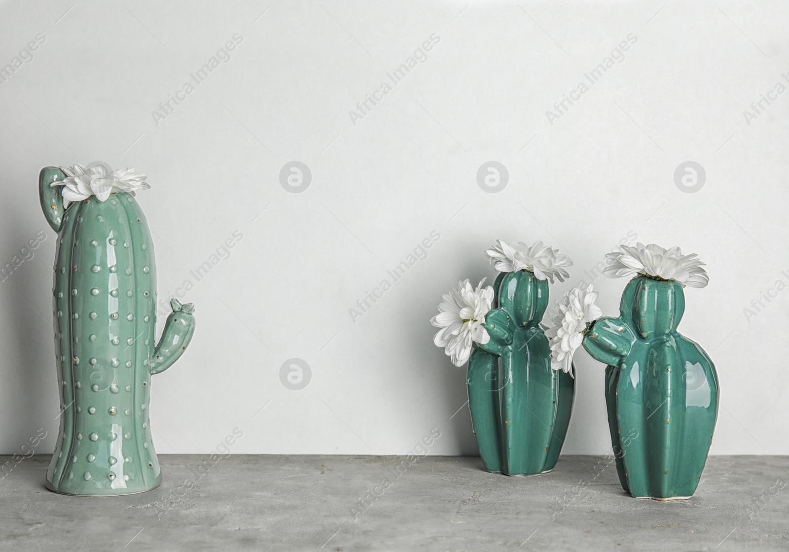 Photo of Trendy cactus shaped vases with flowers on table against light wall. Creative decor