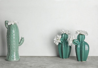 Trendy cactus shaped vases with flowers on table against light wall. Creative decor