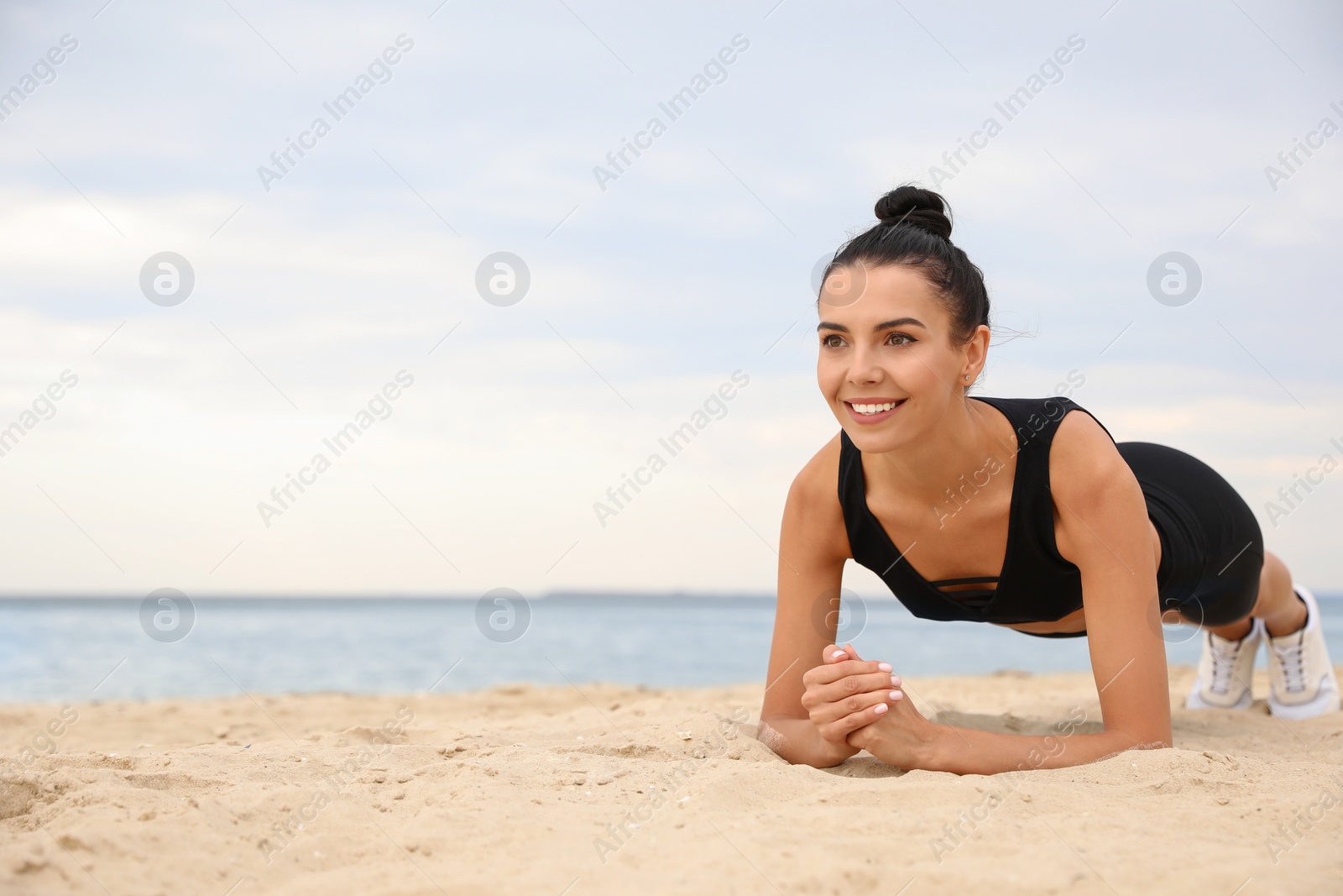 Photo of Young woman doing plank exercise on beach, space for text. Body training