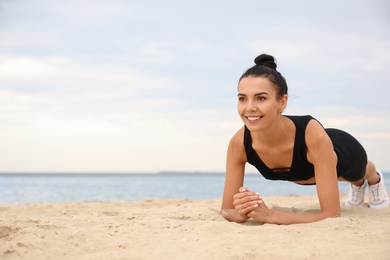 Photo of Young woman doing plank exercise on beach, space for text. Body training