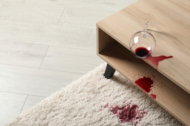 Photo of Overturned glass and spilled red wine on white carpet indoors, space for text
