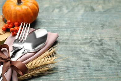 Cutlery with napkin, wheat spikes and pumpkin on blue wooden table, space for text. Thanksgiving Day