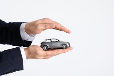 Male insurance agent holding toy car on white background, closeup. Space for text