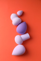 Photo of Many colorful makeup sponges on orange background, flat lay