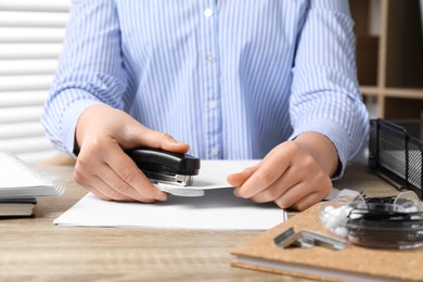 Photo of Woman with papers using stapler at wooden table indoors, closeup