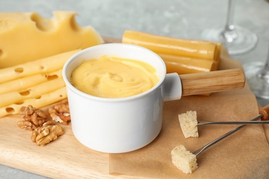 Photo of Pot of tasty cheese fondue served on cutting board