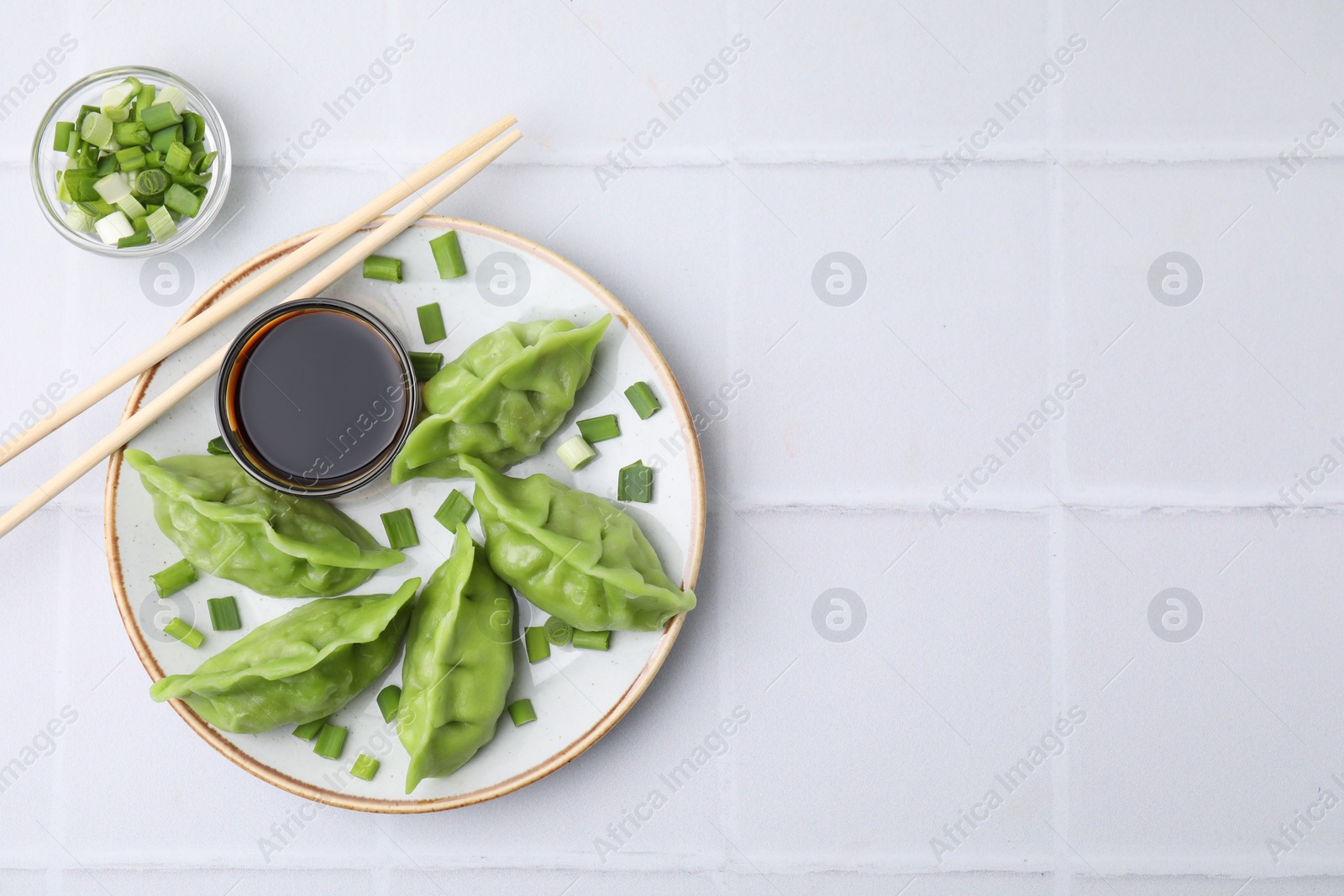 Photo of Delicious green dumplings (gyozas) served on white tiled table, flat lay. Space for text