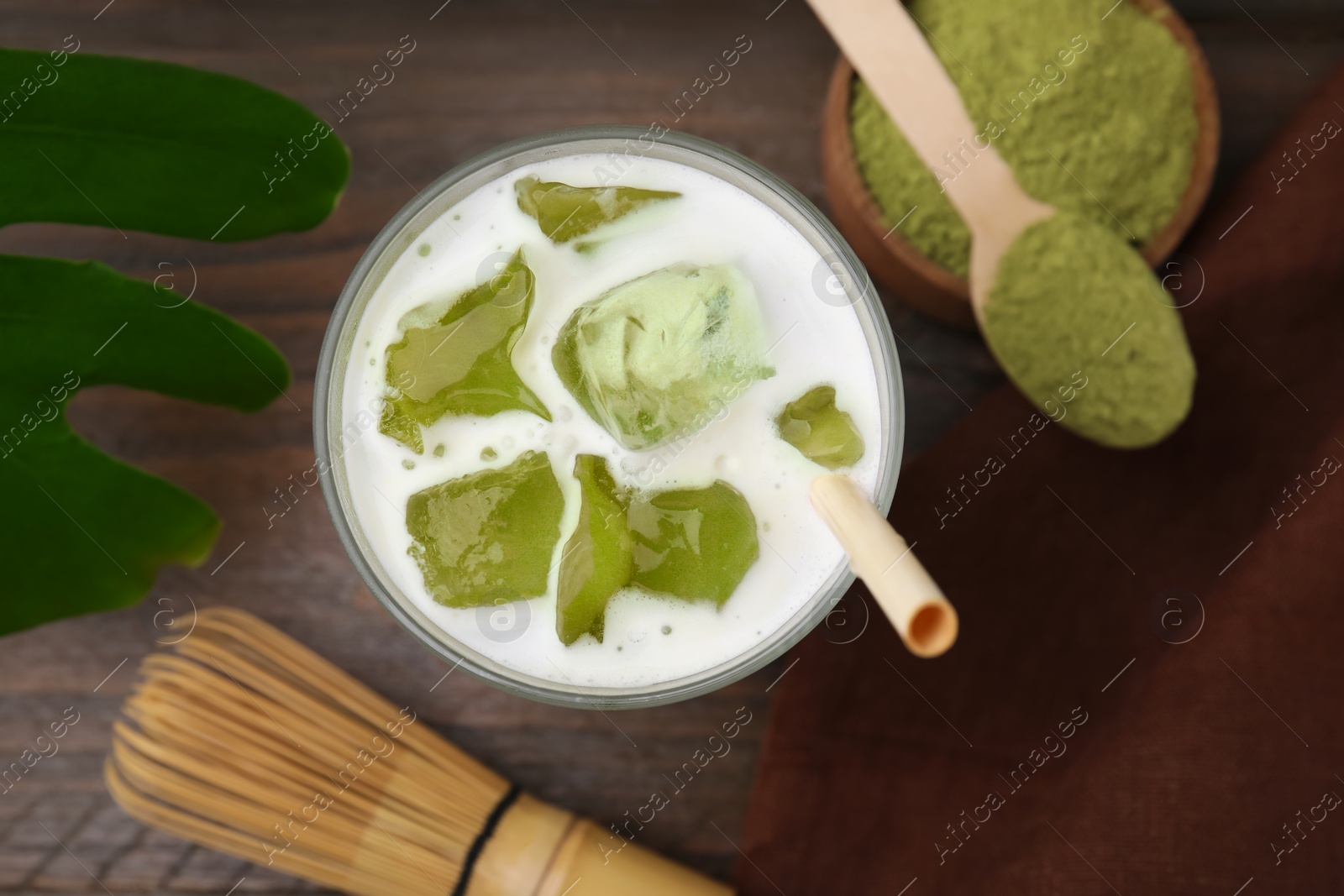 Photo of Glass of tasty iced matcha latte, bamboo whisk and powder on wooden table, flat lay