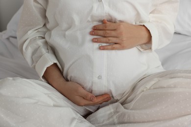 Photo of Pregnant woman in pajamas on bed at home, closeup
