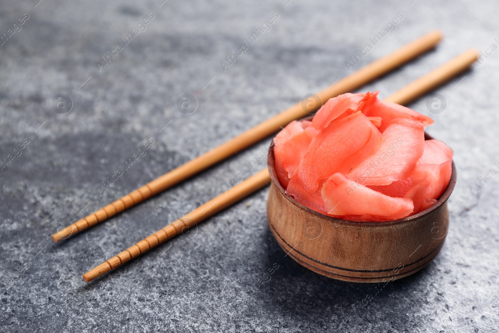 Photo of Pickled ginger in bowl and chopsticks on grey table, space for text