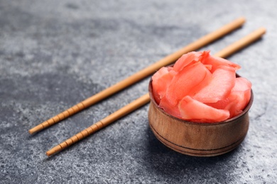 Pickled ginger in bowl and chopsticks on grey table, space for text