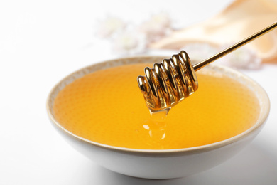 Bowl with organic honey and dipper on white background, closeup