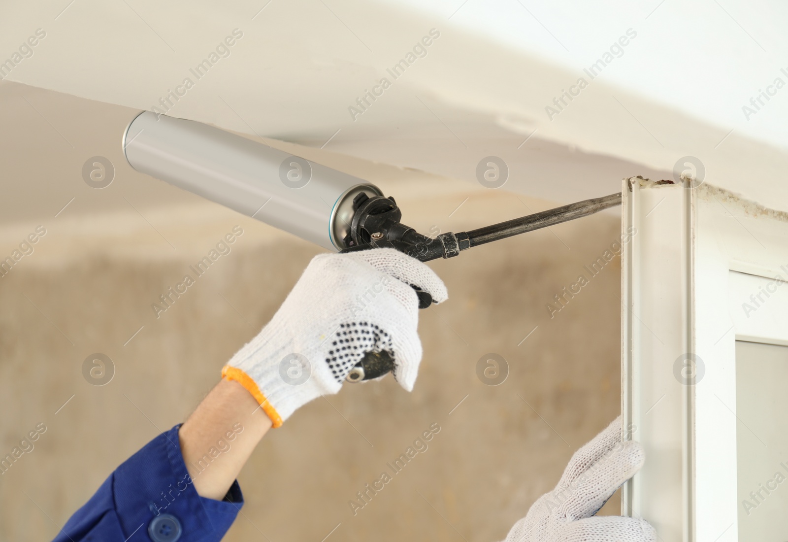 Photo of Worker using foam gun for window installation indoors, closeup