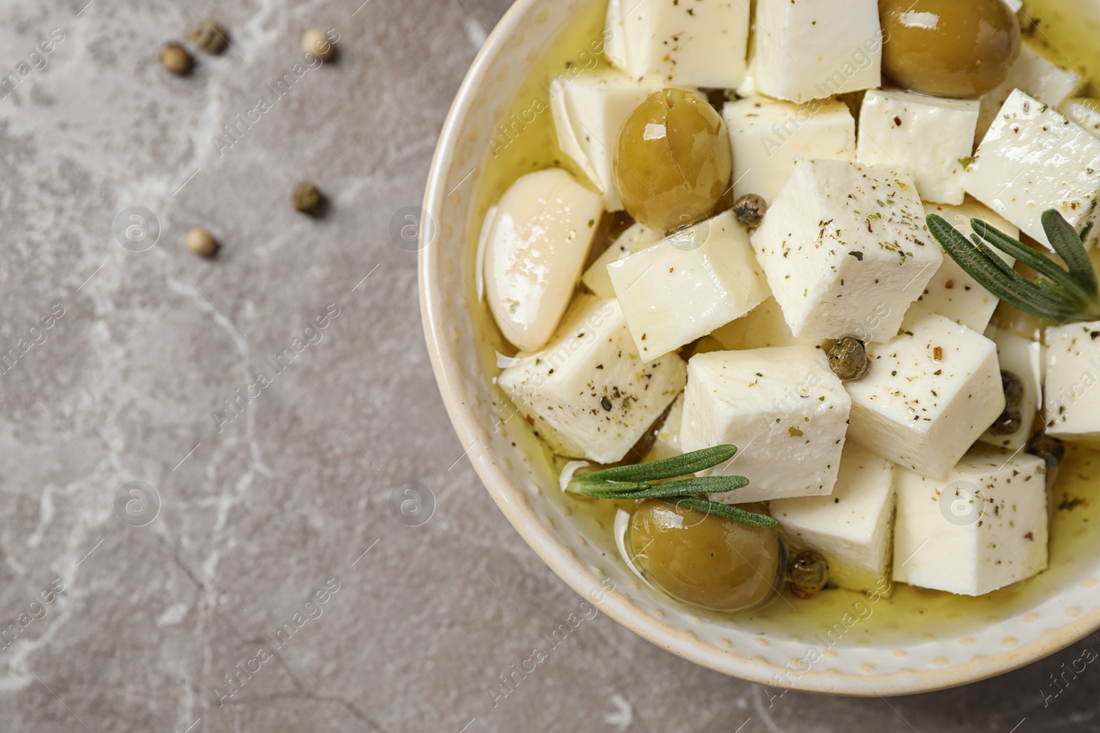 Photo of Pickled feta cheese in bowl on light brown table, top view. Space for text