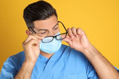Photo of Doctor wiping foggy glasses caused by wearing medical mask on yellow background