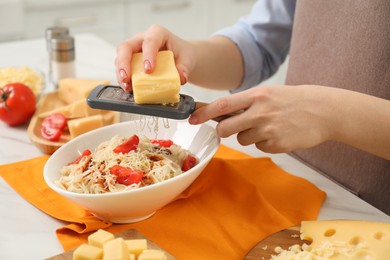 Photo of Woman grating cheese onto delicious pasta at white table indoors, closeup
