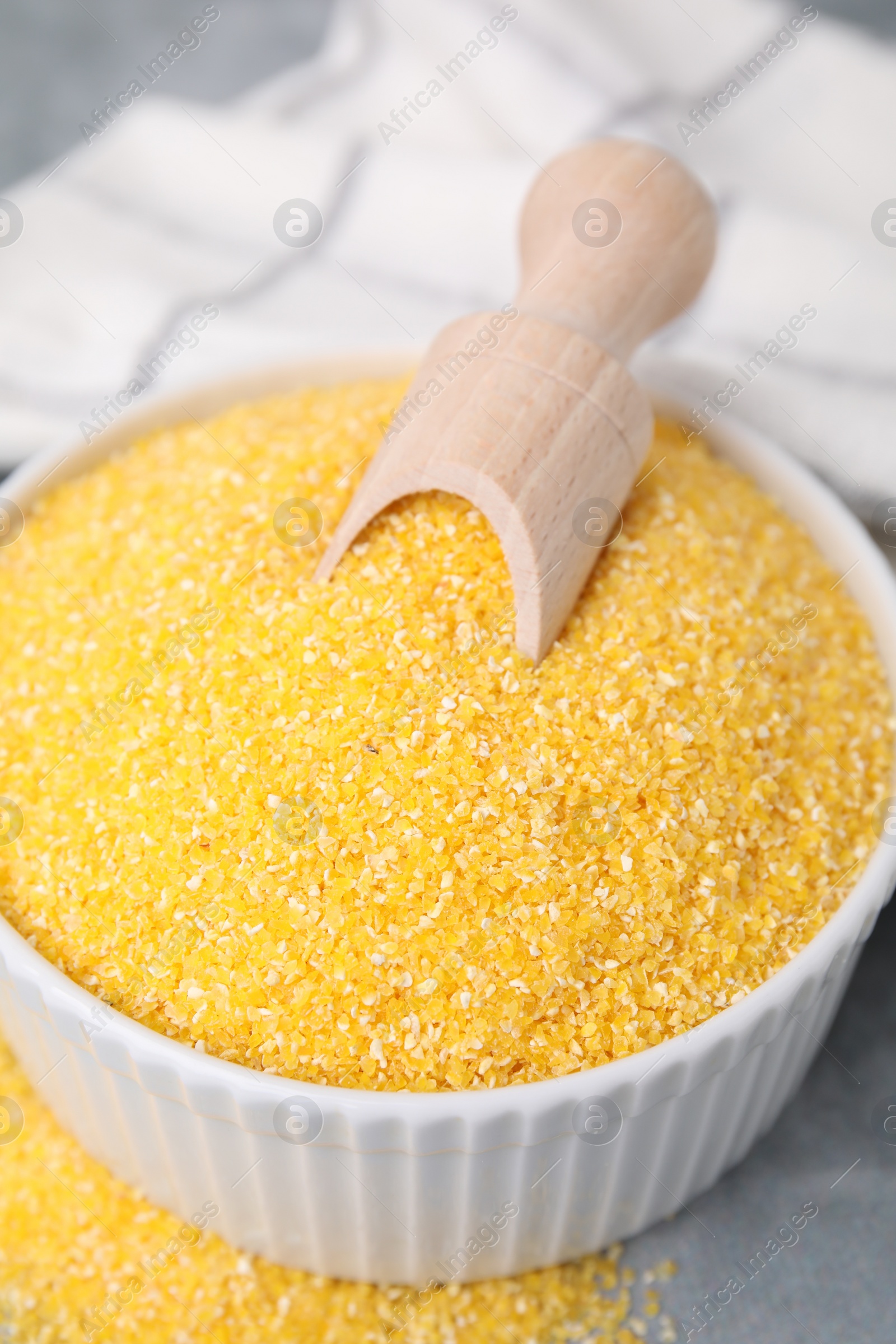 Photo of Raw cornmeal and scoop in bowl on grey table, closeup