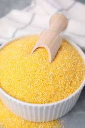 Raw cornmeal and scoop in bowl on grey table, closeup