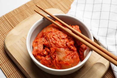 Photo of Bowl of spicy cabbage kimchi with chopsticks on bamboo mat