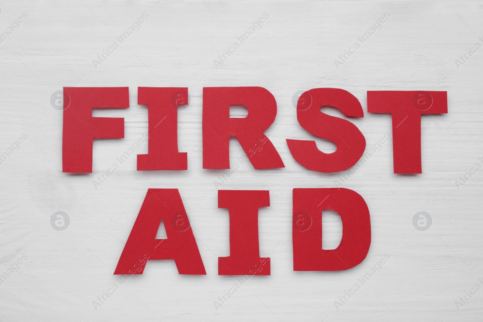 Photo of Words First Aid made of red letters on white wooden table, flat lay