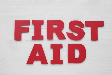 Photo of Words First Aid made of red letters on white wooden table, flat lay